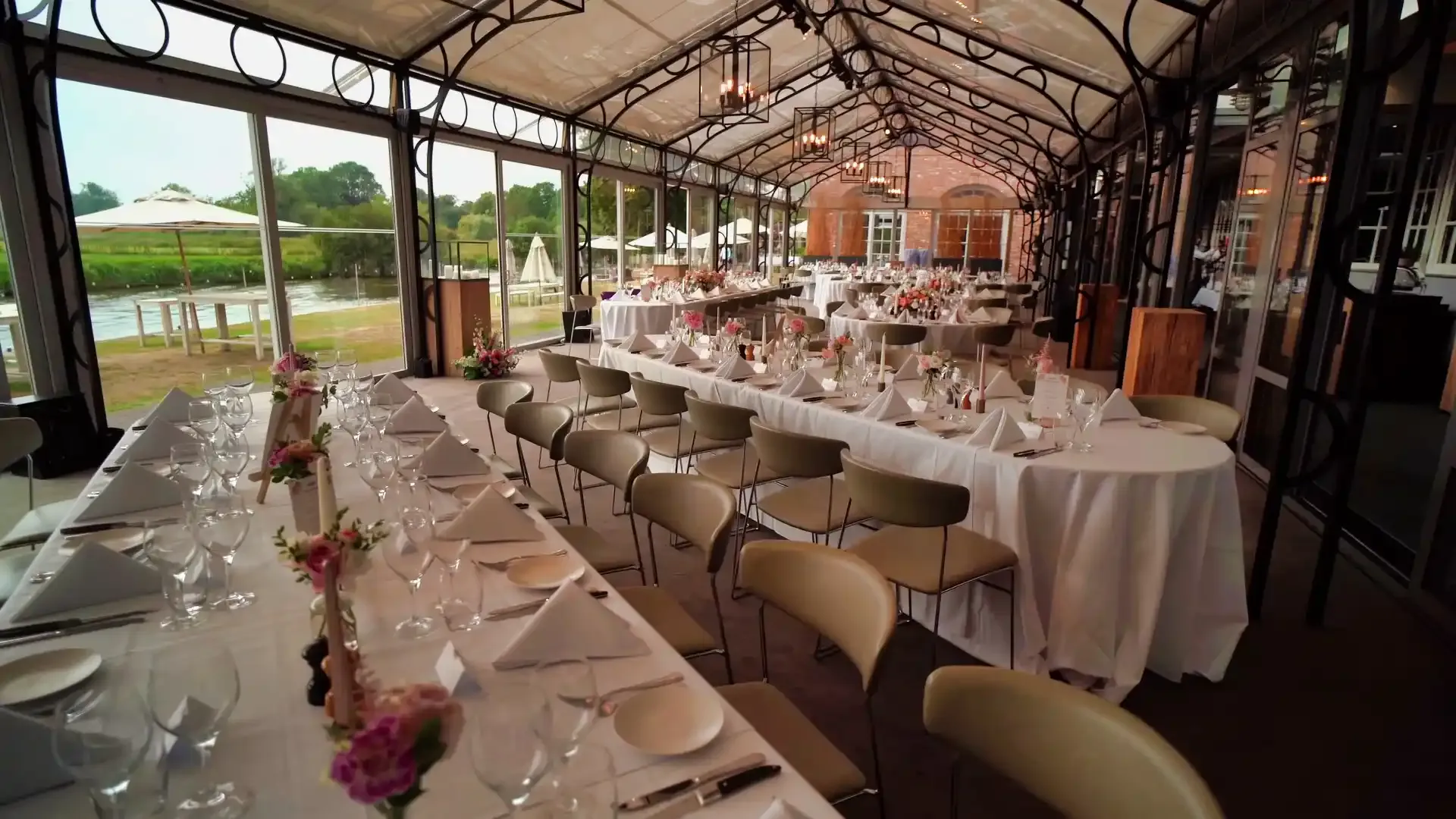Gedekte tafels in een zaal met glazen wanden en dak, met buiten zicht op het water